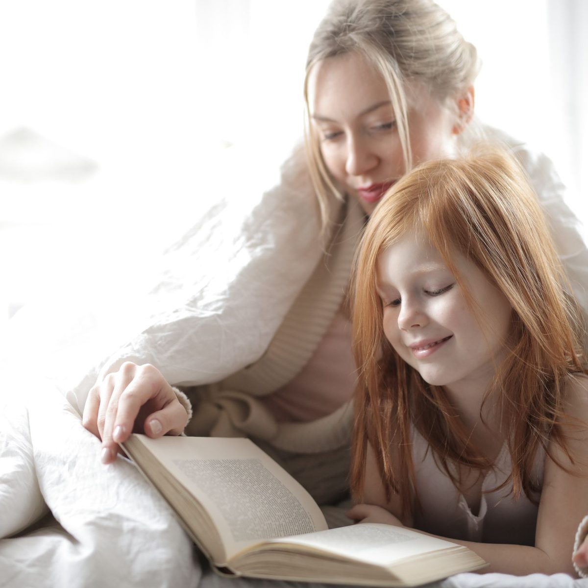 A parent and child reading a book together, wrapped in a soft blanket