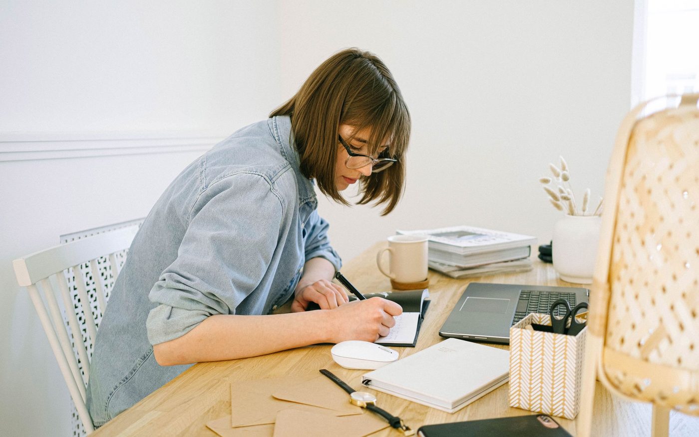 A woman planning at a sunlit desk with a notebook and a cup of coffee